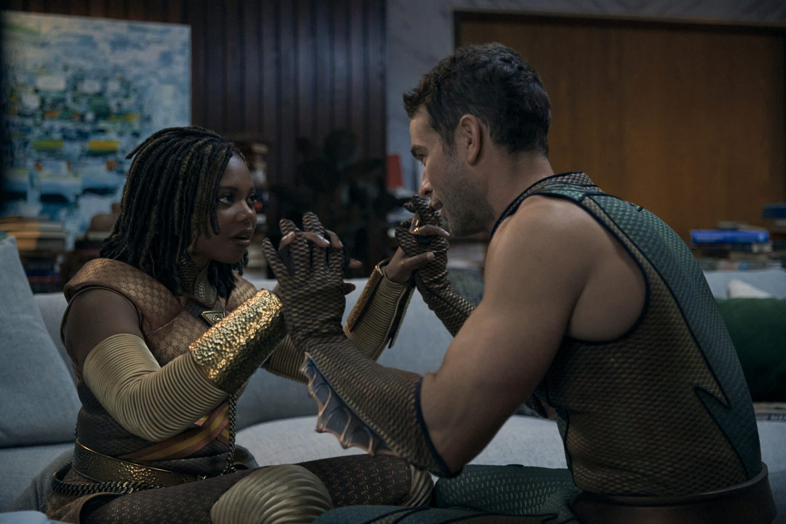 Still from The Boys Season 4 Episode 4, "Wisdom of the Ages," of Susan Heyward as Sister Sage and Chace Crawford as The Deep sitting facing each other holding hands between them, pictured from left to right.