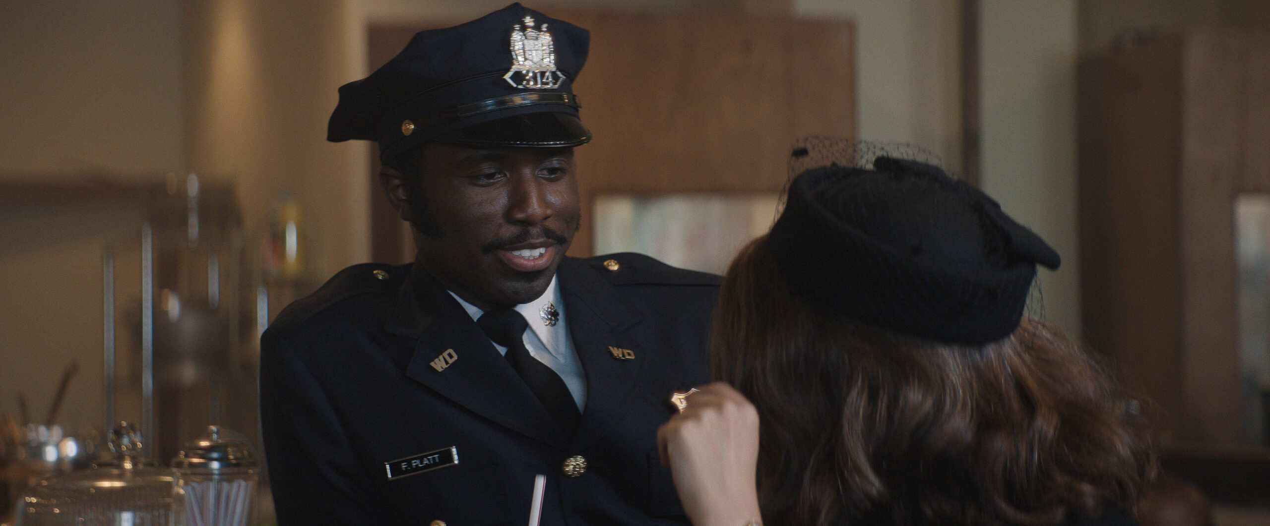 Still from Lady in the Lake Season 1 Episode 1 of Y'lan Noel in a police uniform speaking with a woman who has her back to the camera.