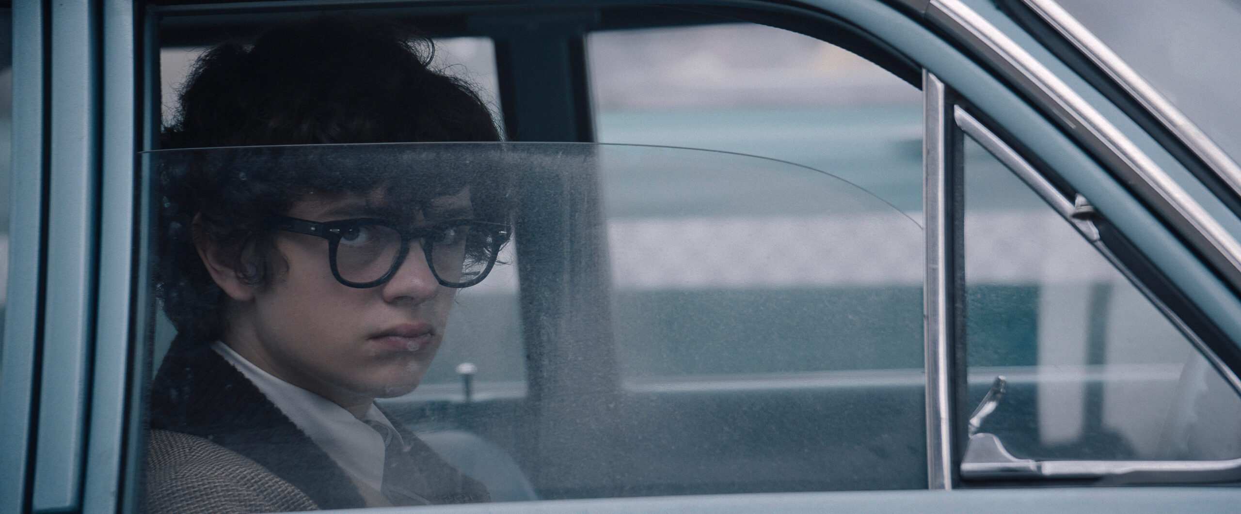 Still from Lady in the Lake Season 1 Episode 3 of Noah Jupe sitting in a care looking out.