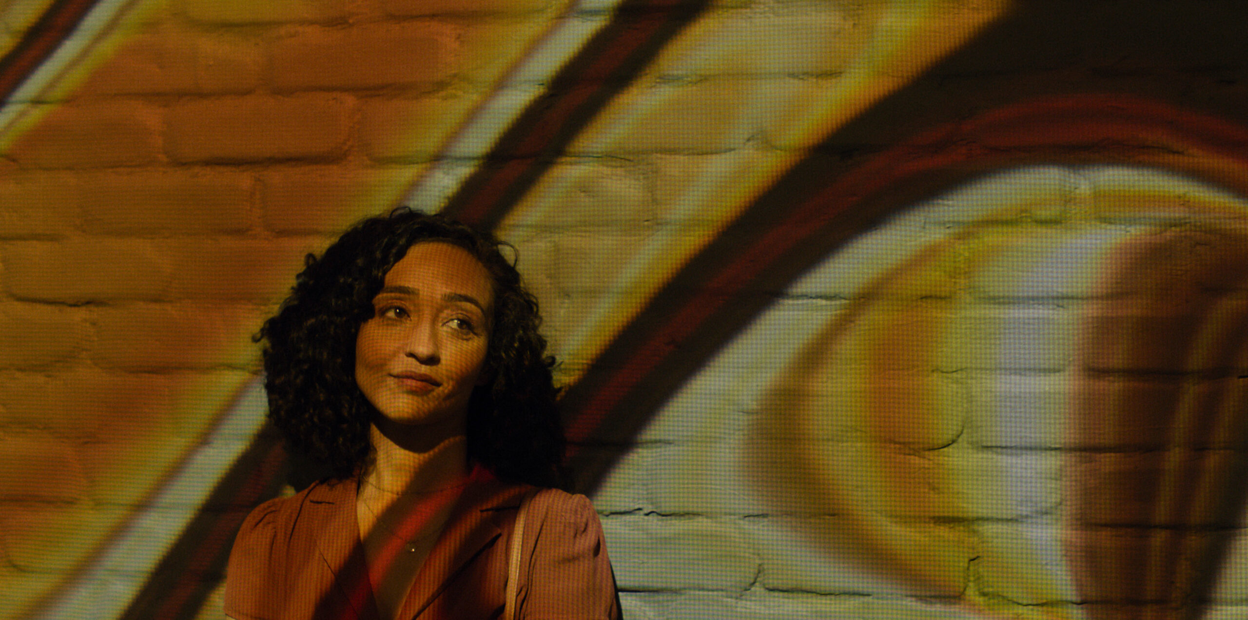 Presumed_Innocent_Photo_010504 | Tell-Tale TV Barbara standing against a wall with colorful lights surrounding her.