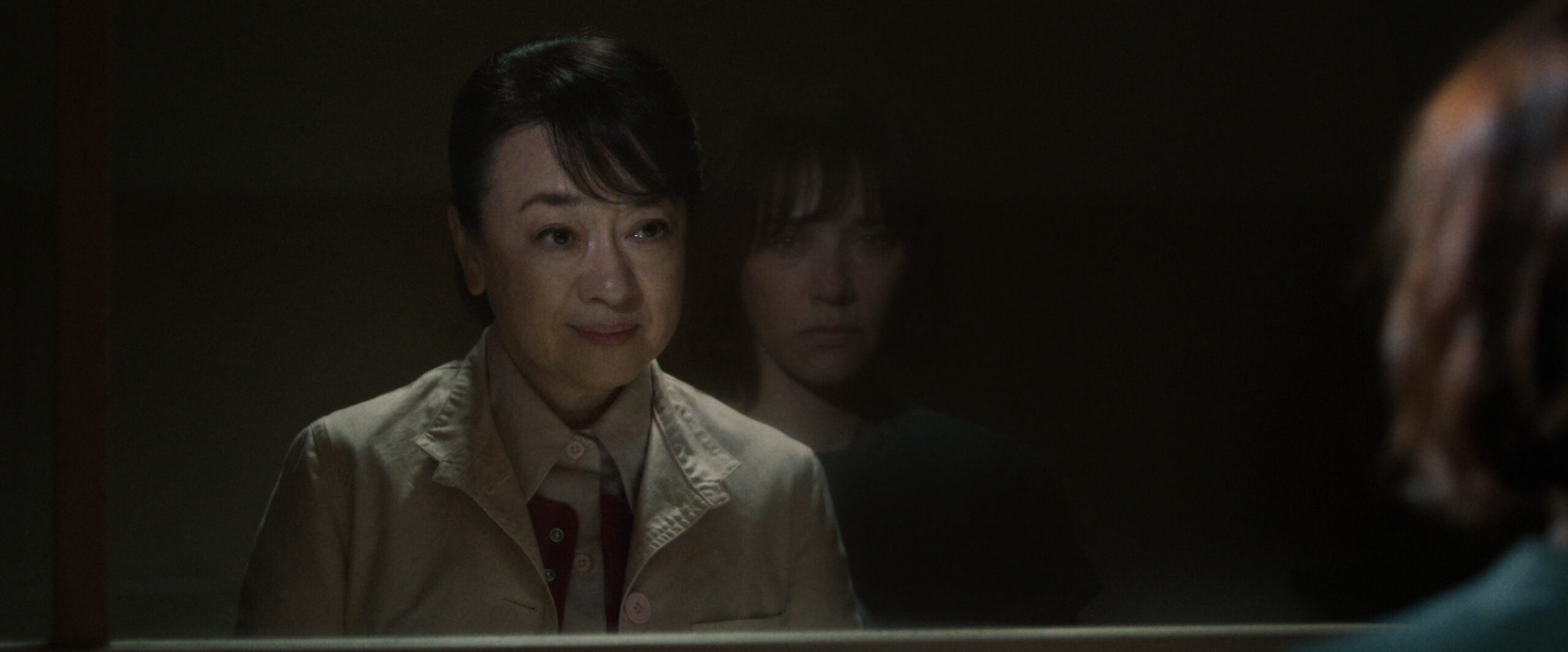 Sunny Season 1 Episode 6 Kyoto Manju So Delicious | Tell-Tale TV Noriko smiles while sitting in a prison visitation station behind glass. We see Suzie's reflection on the other side on Sunny Season 1 Episode 6, "Kyoto Manju So Delicious."