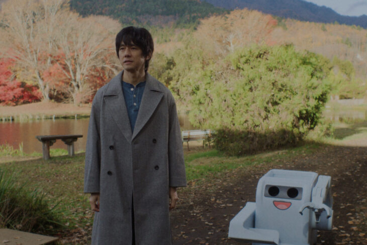 Masa stands outside a cabin in the countryside during autumn beside a short, white, boxy robot on Sunny Season 1 Episode 8, "Trash or Not-Trash."