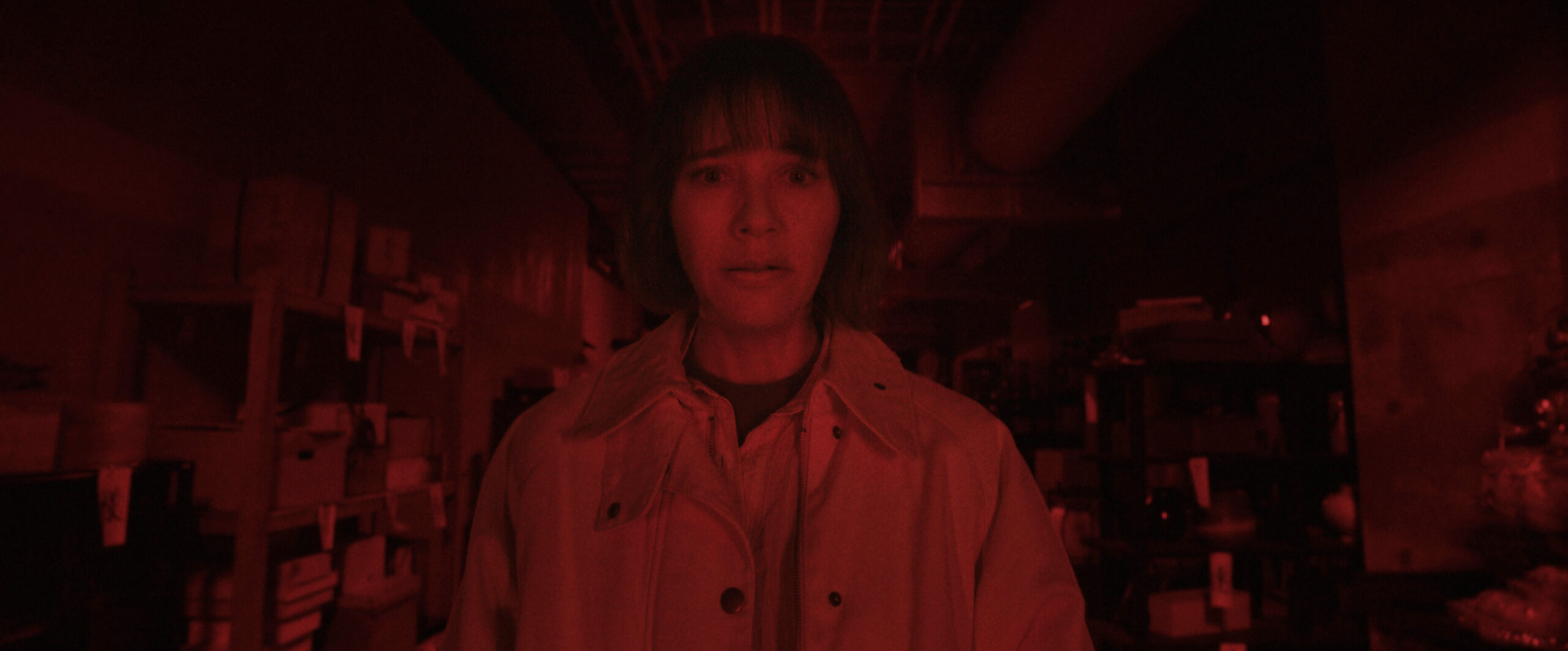 Sunny Season 1 Episode 8 Trash or Not-Trash | Tell-Tale TV Suzie stands in a warehouse-type space while looking shocked and washed in a dark red filter on Sunny Season 1 Episode 8, "Trash or Not-Trash."