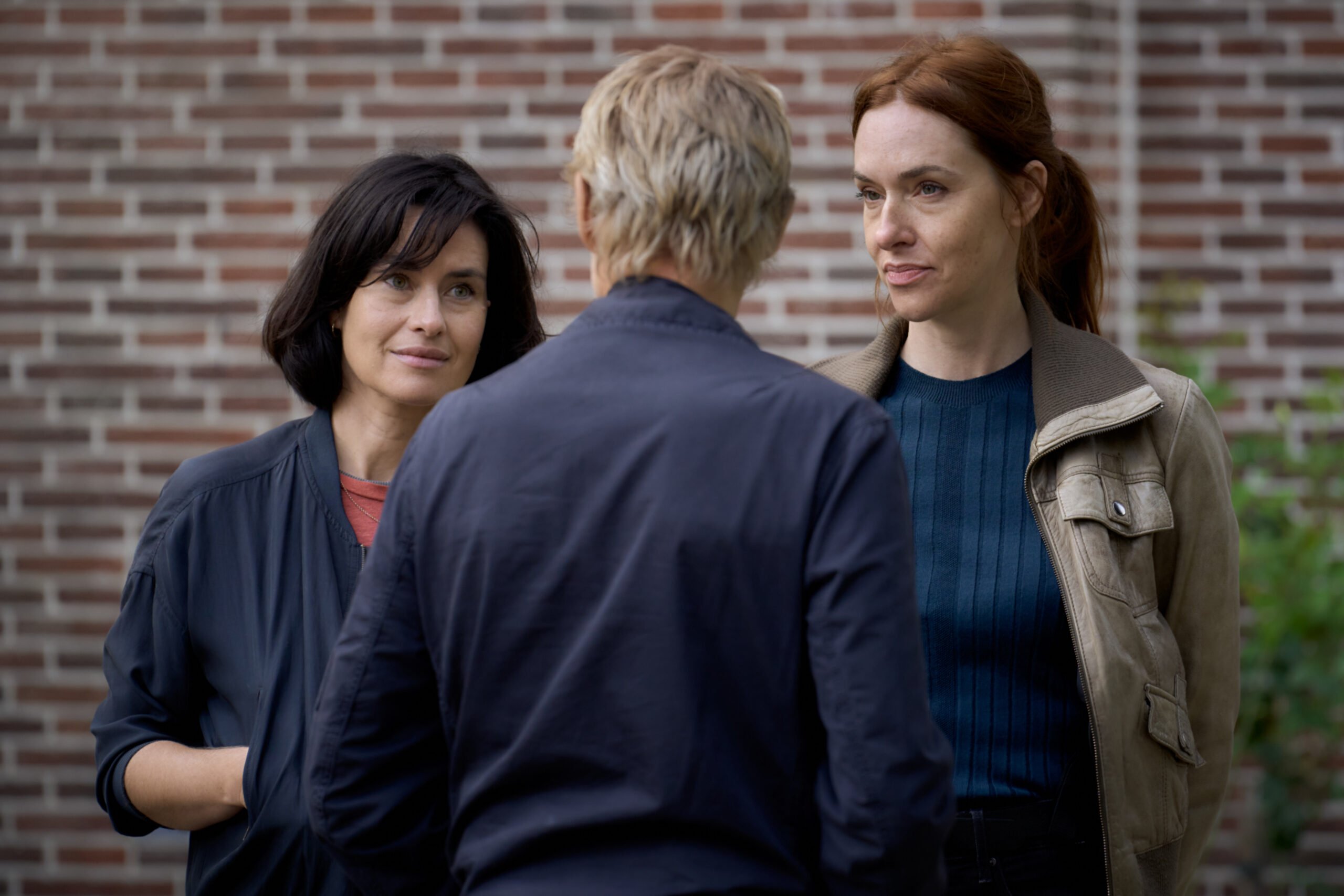 VAN DER VALK SEASON 4 ON MASTERPIECE Lucienne Hassell, Piet Van der Valk, Kalie_ | Tell-Tale TV Still from Van der Valk Season 4 Episode 2 of Maimie McCoy as Lucienne Hassell, Marc Warren as Piet Van der Valk, and Kim Riedle as Kalie pictured from left to right.