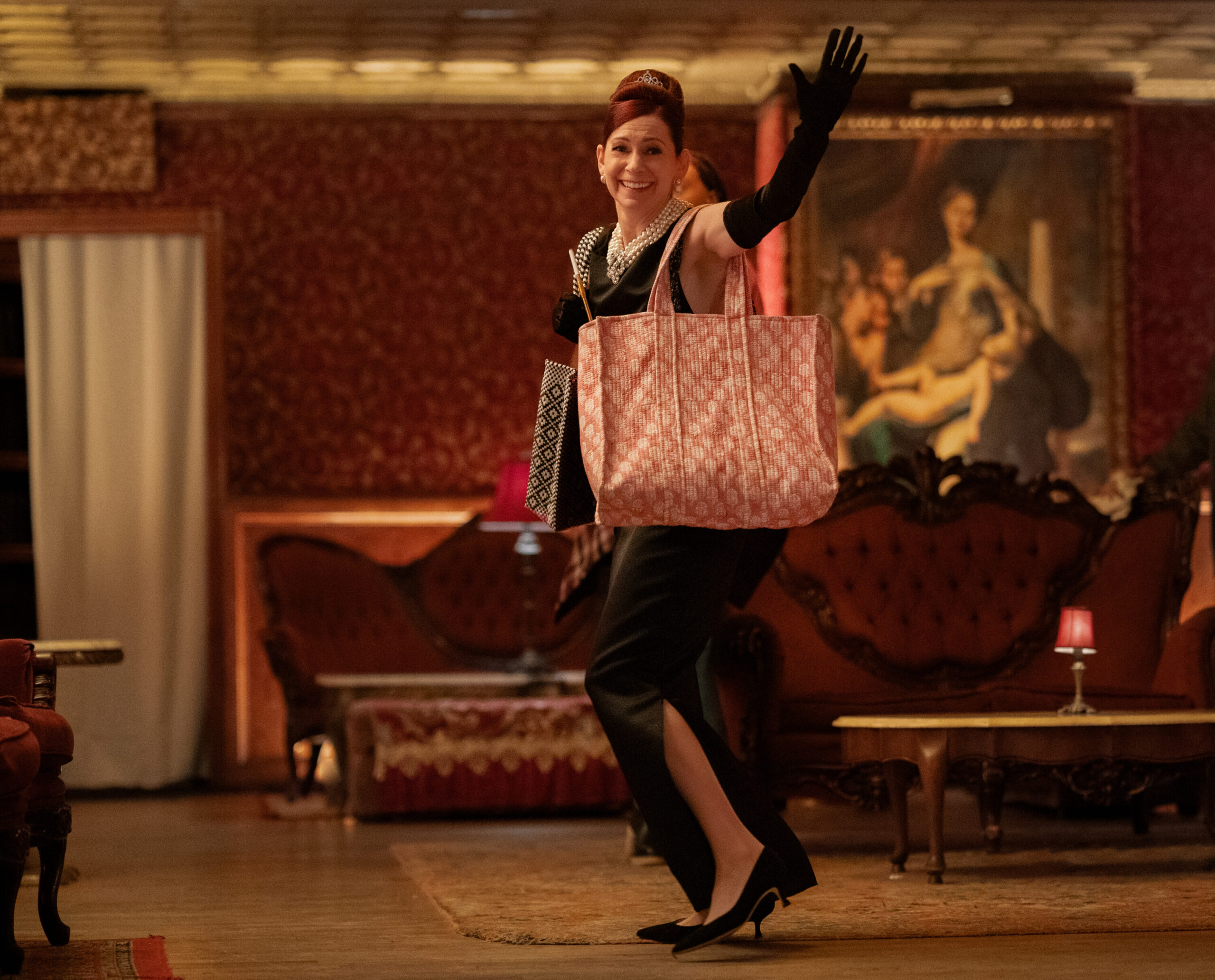 Still from Elsbeth Season 2 episode 3 of Carrie Preston dressed as Holly Golightly from Breakfast at Tiffany's carrying a large red and white bag.
