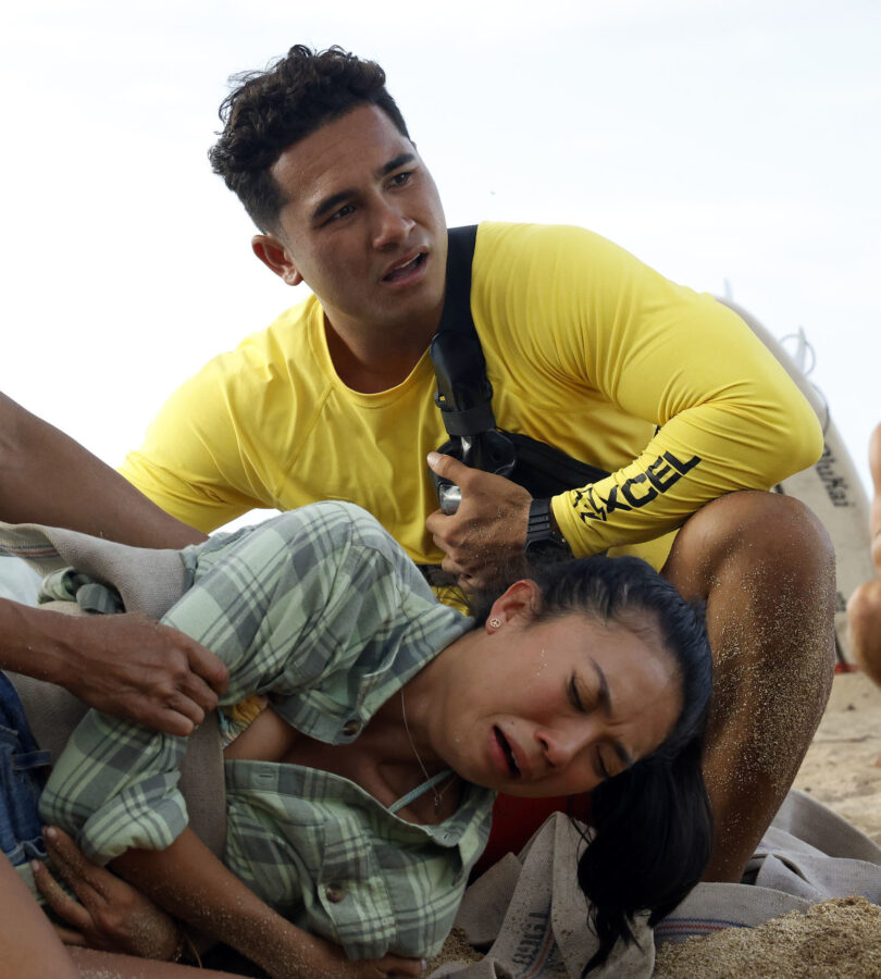 RESCUE: HIGH SURF Season 1 Episode 4 - Kekoa Kekumano | Tell-Tale TV Still from RESCUE: HIGH SURF Season 1 Episode 4 of Kekoa Kekumano pictured at the top of the photo leaning over an injured woman at the bottom of the photo.