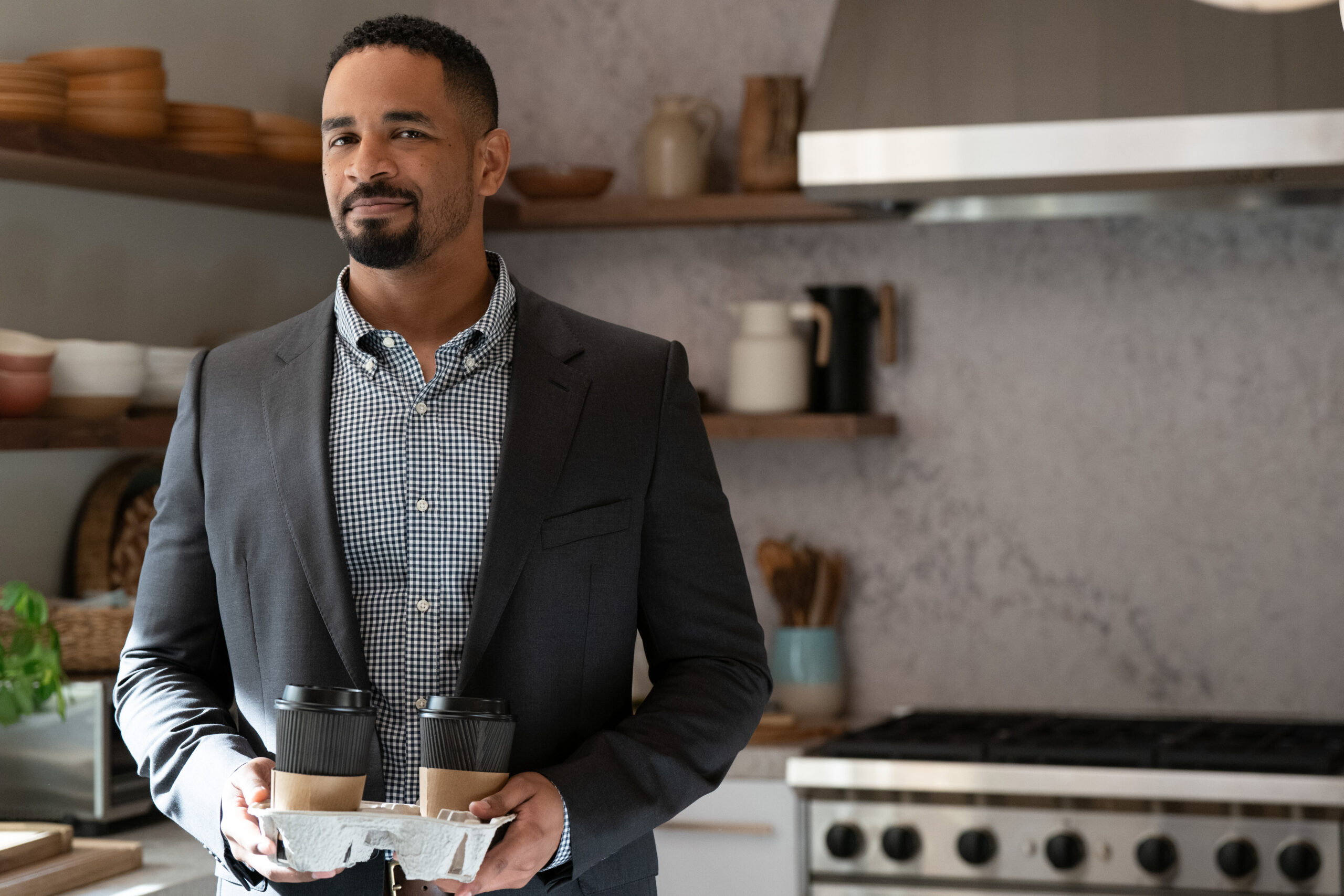 Shrinking Season 2 Episode 4 Made You Look (4) | Tell-Tale TV Derrick stands in a kitchen during the day while smiling on Shrinking Season 2 Episode 4, "Made You Look."