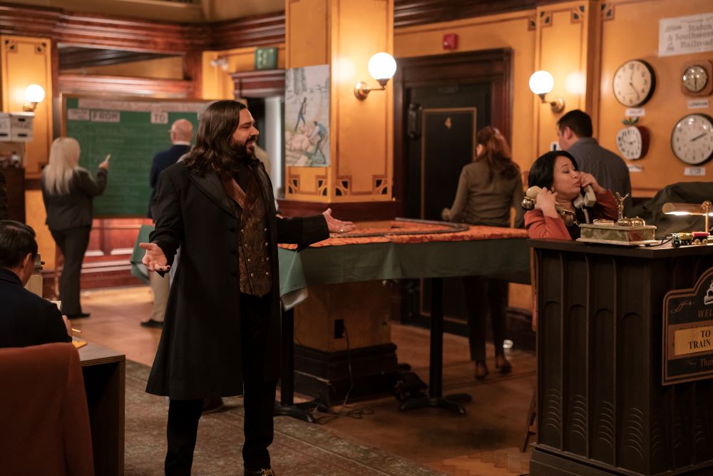 Laszlo gestures wildly and smiles while standing in the office of a railroad company on What We Do in the Shadows Season 6 Episode 4, "The Railroad."