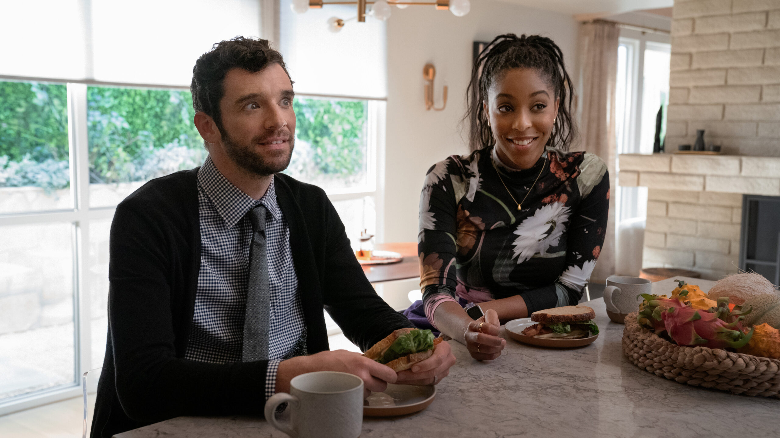 Shrinking Season 2 Episode 8 Last Drink | Tell-Tale TV Brian and Gaby sit at a kitchen island while smiling and engaging with someone off-screen on Shrinking Season 2 Episode 8, "Last Drink."