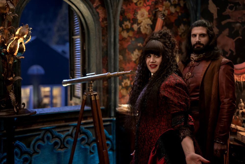 Nadja and Nandor stand in front of a telescope in a dimly lit room on What We Do in the Shadows Season 6 Episode 6, "Laszlo's Father."