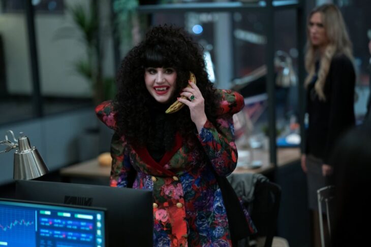 Nadja grins while holding a banana up to her face like a phone and standing in an office on What We Do in the Shadows Season 6 Episode 7, "March Madness."