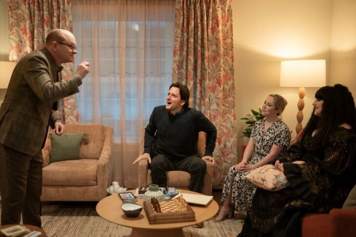 Colin Robinson performs charades while standing in a living room. Joel, Becky, and Nadja sit on chairs in front of him on What We Do in the Shadows Season 6 Episode 8, "P.I. Undercover New York."