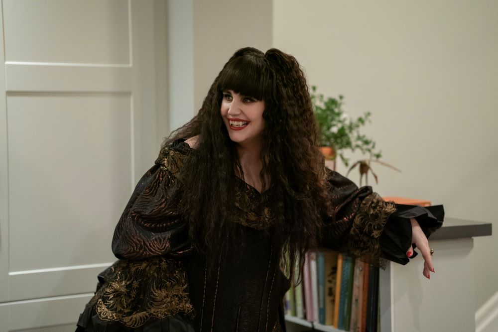What We Do in the Shadows Season 6 Episode 8 P.I. Undercover New York (3) | Tell-Tale TV Nadja smiles while standing in the den of a home and leans on a bookcase on What We Do in the Shadows Season 6 Episode 8, "P.I. Undercover New York."