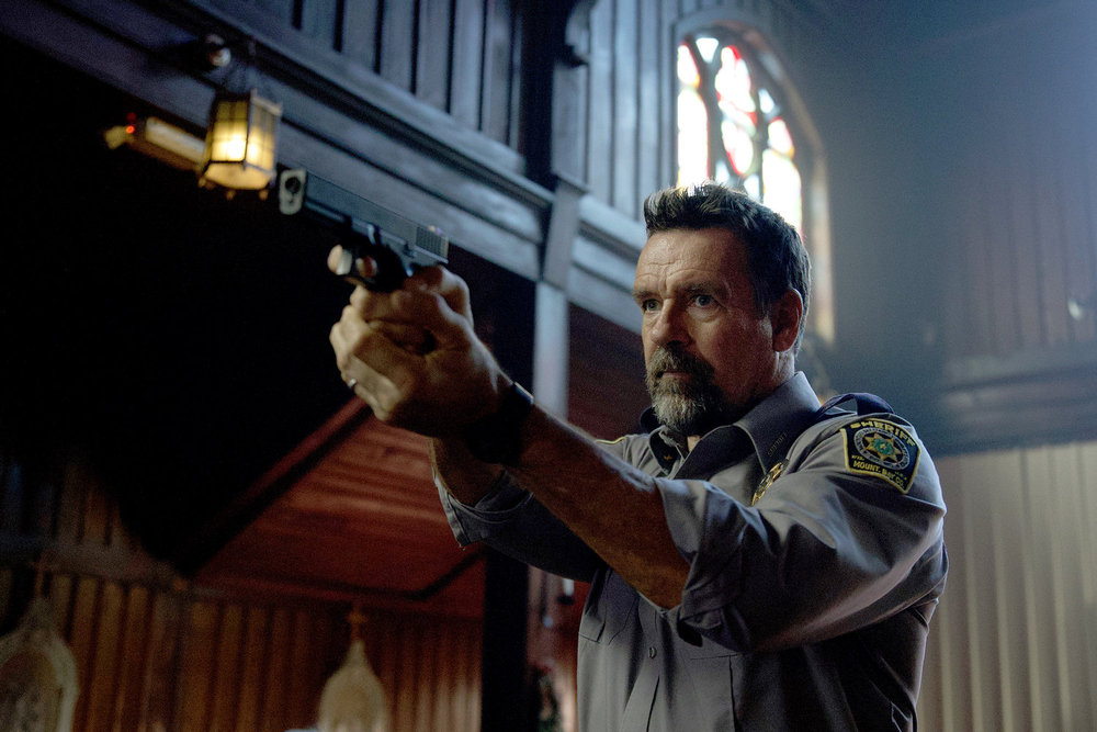 Still from Revival Season 1 Episode 3 of David James Elliott as Sheriff Wayne Cypress holding a gun.