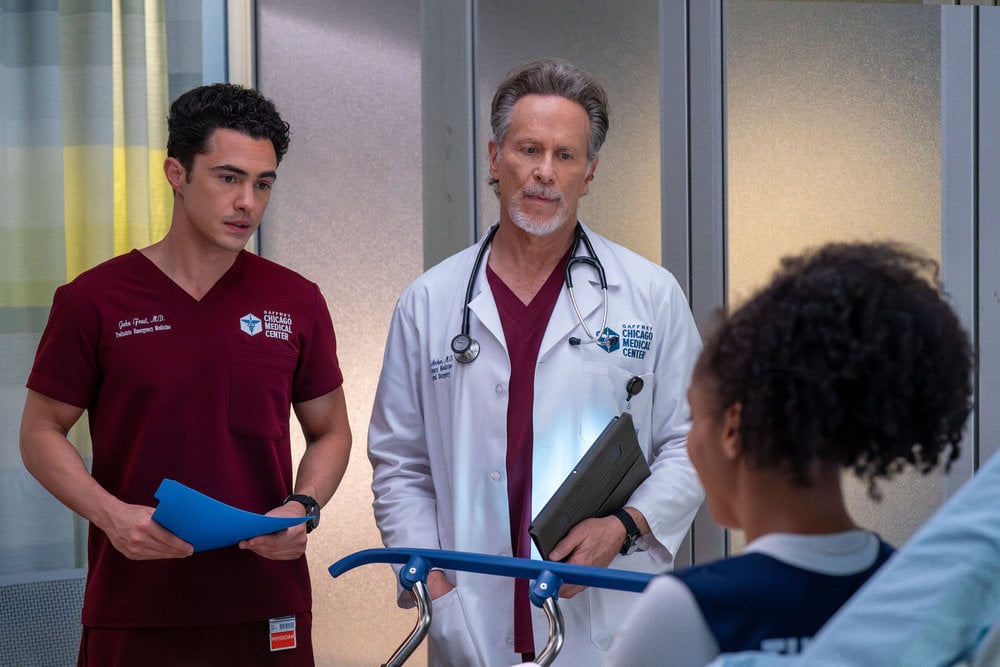 Darren Barnett como Dr. John Frost, Steven Webber como Dr. Dean Archer, parado em um quarto de hospital.