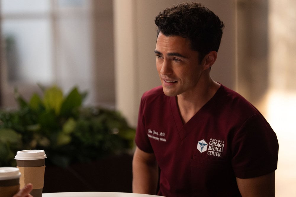 Darren Barnett como Dr. John Frost, sentado no refeitório do pronto-socorro.