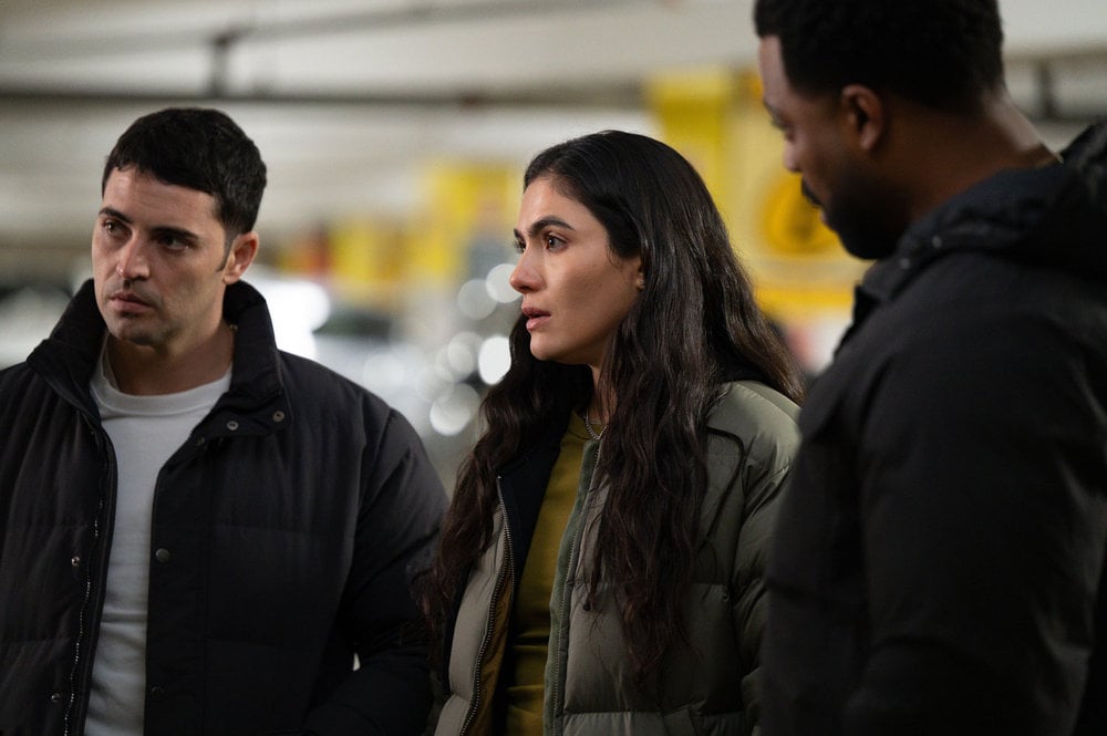 Benjamin Levi Aguilar como Dante Torres, Ariane Mandi como Eva Imani, parados no estacionamento.